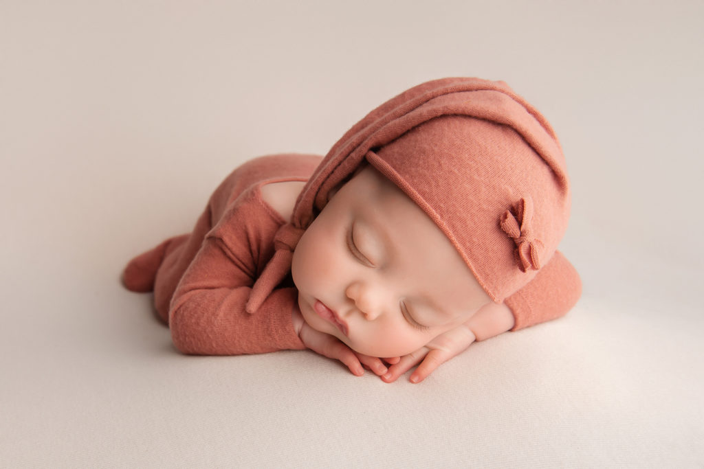 baby girl lays in orange newborn outfit for Las Vegas Studio newborn portraits